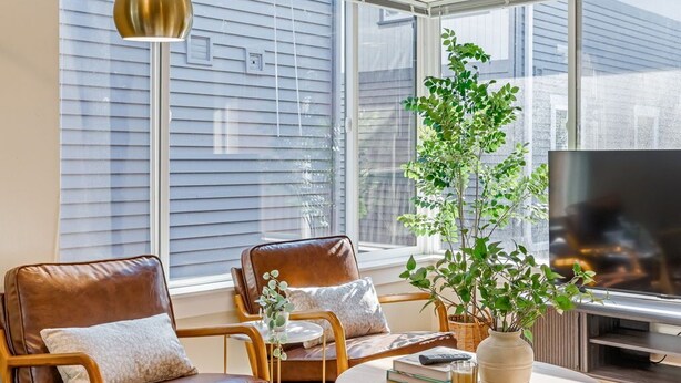 A living room with a sofa, chairs, a coffee table, a TV, and a large window with blinds. - Designated Parking · AC · Walks to Space Needle/DT (Seattle)