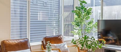 A living room with a sofa, chairs, a coffee table, a TV, and a large window with blinds.