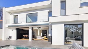 Une maison moderne à deux étages, dotée d’une piscine, de grandes fenêtres et d’un balcon.