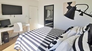 Une chambre à coucher avec un lit, un bureau avec un ordinateur, une télévision et un miroir.