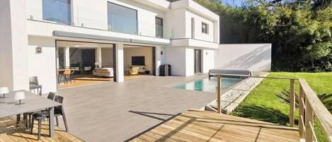 A modern two-story house with a deck, a swimming pool, and a well-maintained lawn.