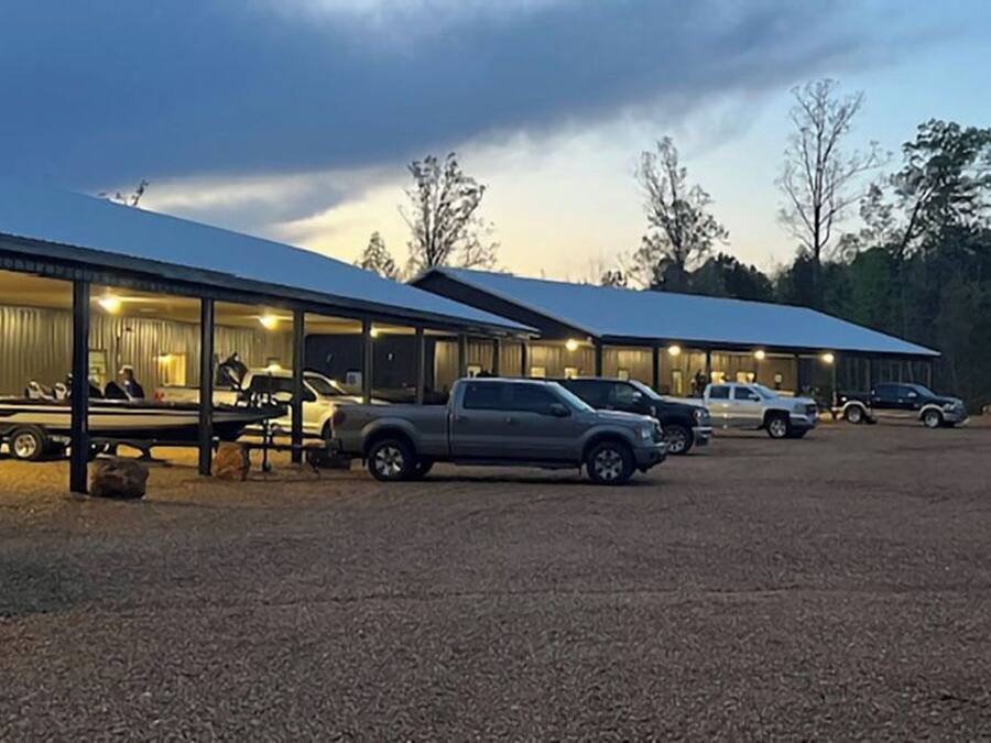 A hotel with multiple rooms, a covered parking area, and a gravel ground.