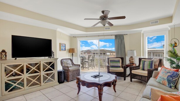 A living room with a TV, wicker furniture, a ceiling fan, and a balcony with a view. - Ocean‑View Condo in Beachside Colony • Pools • Steps to the Sand • Restaurant (Tybee Island)