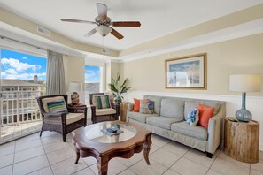 A living room with a ceiling fan, a sofa, a coffee table, and a view of the outside. - Ocean‑View Condo in Beachside Colony • Pools • Steps to the Sand • Restaurant (Tybee Island)