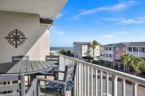 Een balkon met een tafel en stoelen, een kompas decoratie, en uitzicht op gebouwen en palmbomen.