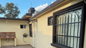 A covered outdoor area with a tiled floor, a bench, a water tap, a window with a metal grill, and a water tank. - LOFT SN1 FOR 2 PEOPLE WITH PARKING AND AMENITIES (San Nicolás de los Garza)