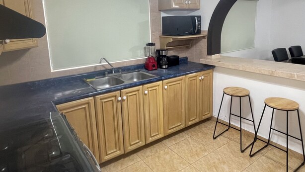 A kitchen with a sink, countertop, wooden cabinets, a microwave, and two stools. - LOFT SN1 FOR 2 PEOPLE WITH PARKING AND AMENITIES (San Nicolás de los Garza)
