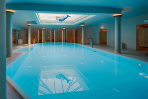 Una amplia piscina interior con techo de tragaluces, columnas y vista al cielo.