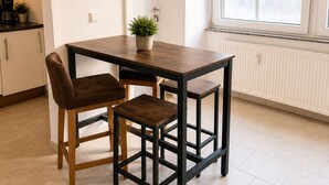 Un comedor con una mesa, dos sillas, una planta en maceta, una ventana con persianas y un radiador.