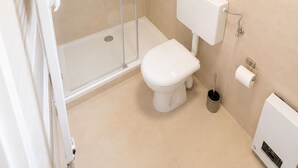 Un baño moderno con cabina de ducha de vidrio, inodoro, lavabo y ventana con planta.