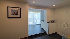 Quarto moderno com área de jantar, um quadro na parede, uma porta que dá para uma varanda e uma pequena estante com objetos.