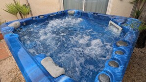 Uma banheira de hidromassagem com exterior azul, rodeada por um espaço de pátio com telhado de azulejos e uma porta de correr de vidro.