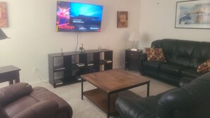 Een woonkamer met een televisie, een zwarte leren bank, een houten salontafel en een zwarte tv-kast.