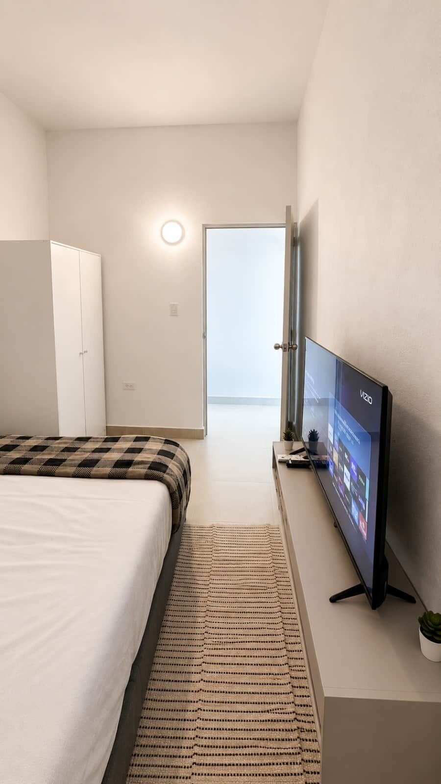 Quarto de hotel com cama, televisão, uma pequena planta e vista para o exterior.
