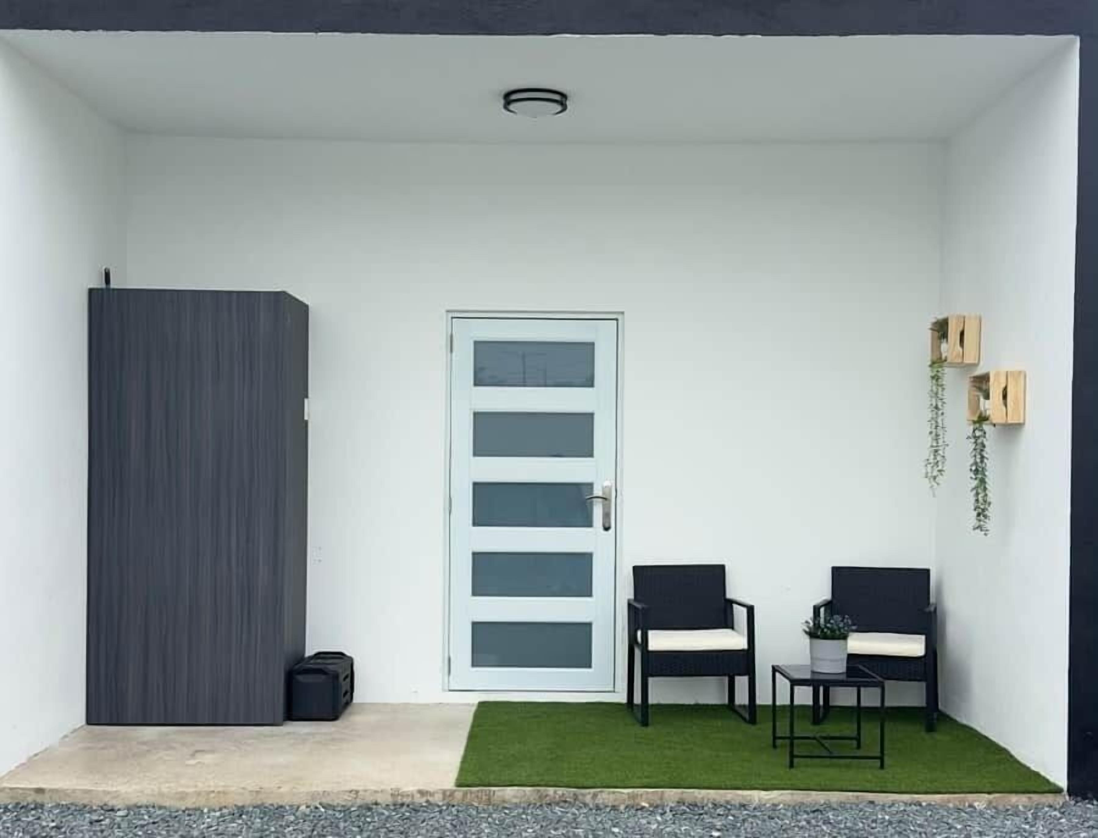 A small, enclosed outdoor area with a white door, two chairs, a small table, and a potted plant.