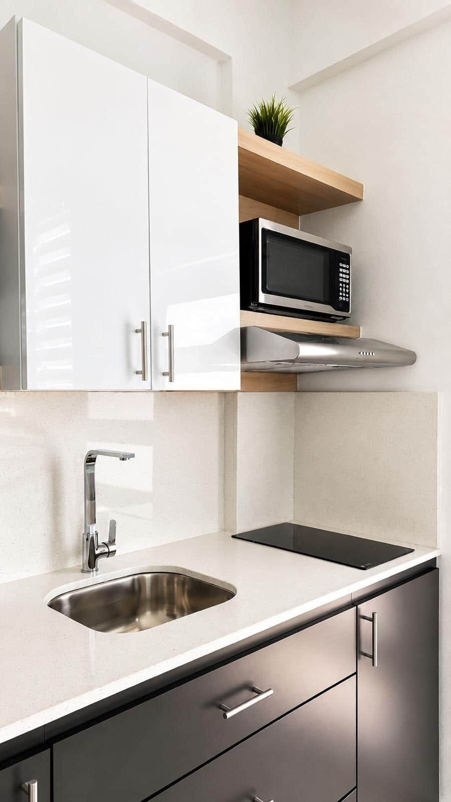 A modern kitchen with stainless steel appliances, a sink, and a wooden shelf with a plant.