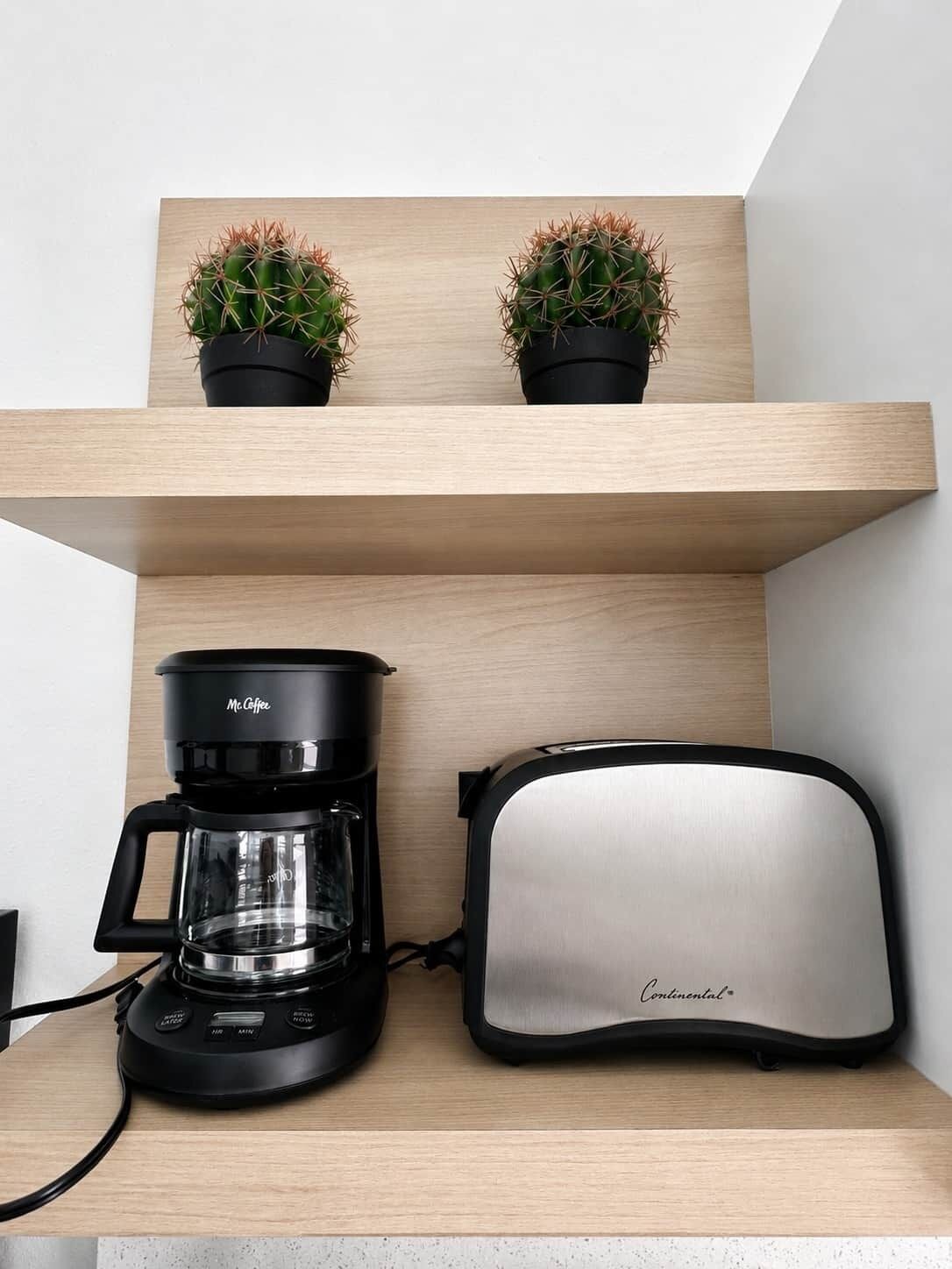 A kitchen with a coffee maker, toaster, and two potted plants on a wooden shelf.