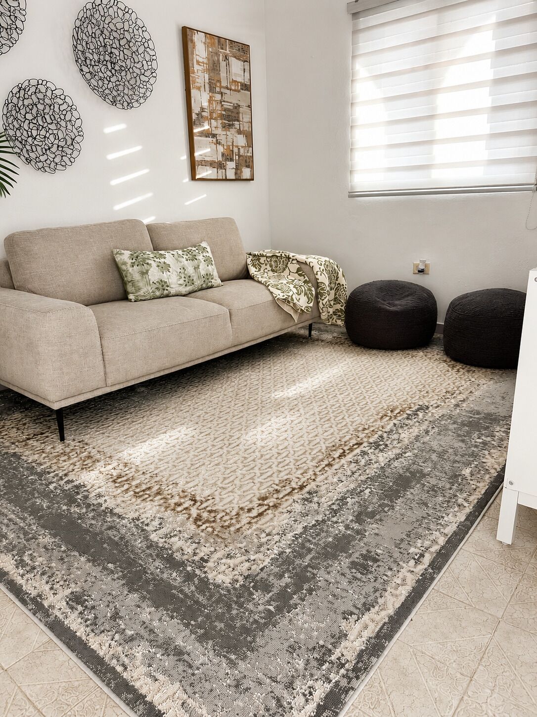A living room with a sofa, ottomans, a patterned rug, and wall art.