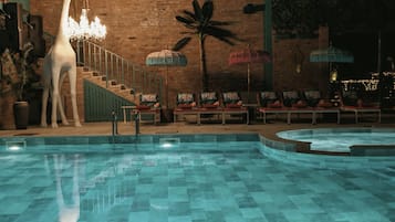 Piscina interna com piso ladrilhado, estátua de girafa e cadeiras de descanso.