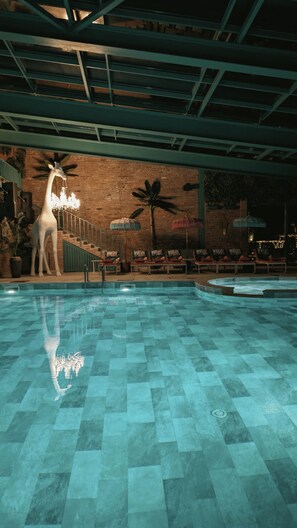 An indoor swimming pool with a tiled floor, a giraffe statue, and lounge chairs.