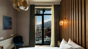Habitación de hotel con cama, una silla, un balcón y vistas a las montañas, además de una lámpara colgante.