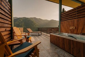 A wooden deck with a hot tub and lounge chairs overlooking a mountainous landscape.