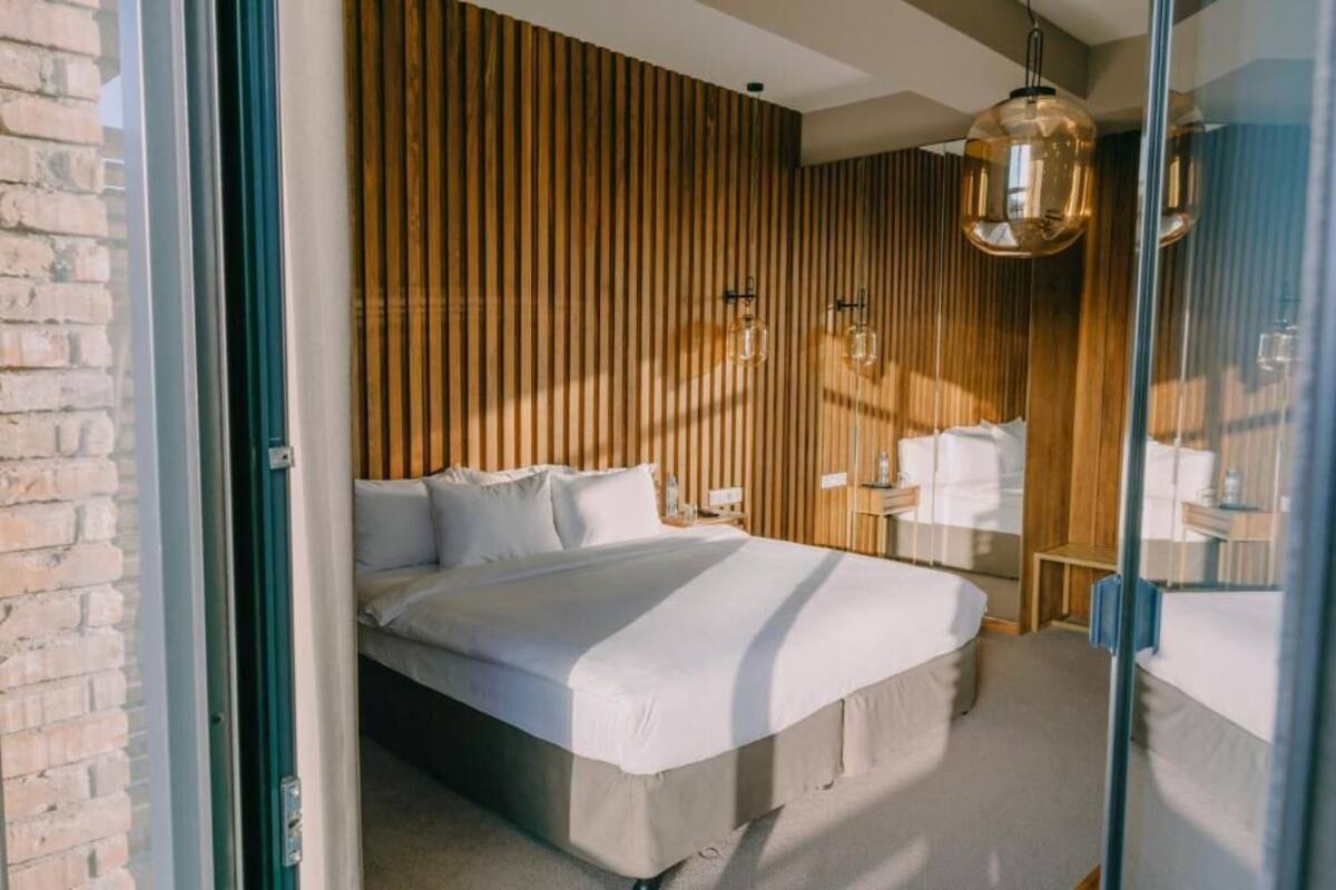 A modern bedroom with a large bed, wooden panel wall, and a hanging light fixture.