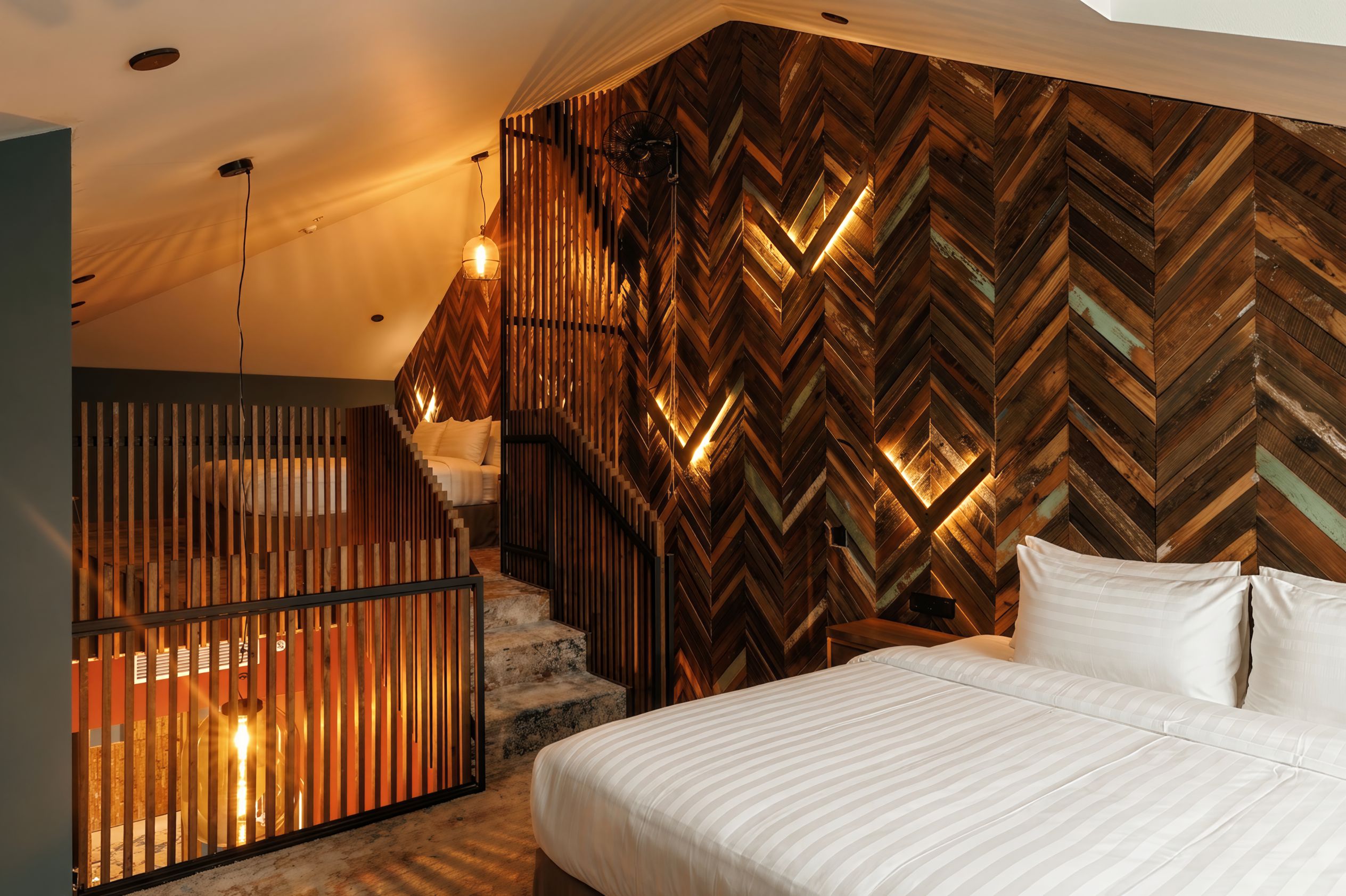 A bedroom with a herringbone-patterned wall, a bed with white bedding, and a staircase with wooden railings.