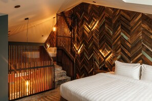 A bedroom with a herringbone-patterned wall, a bed with white bedding, and a staircase with wooden railings.
