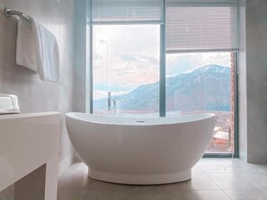 Un baño moderno con una bañera independiente, un lavabo blanco y un amplio ventanal con vistas a la montaña.