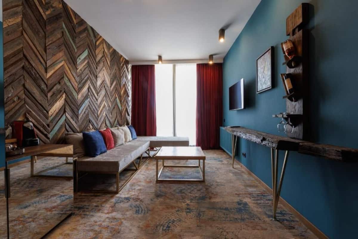 A modern living room with a herringbone wood wall, a sofa with cushions, a coffee table, and a TV mounted on the wall.