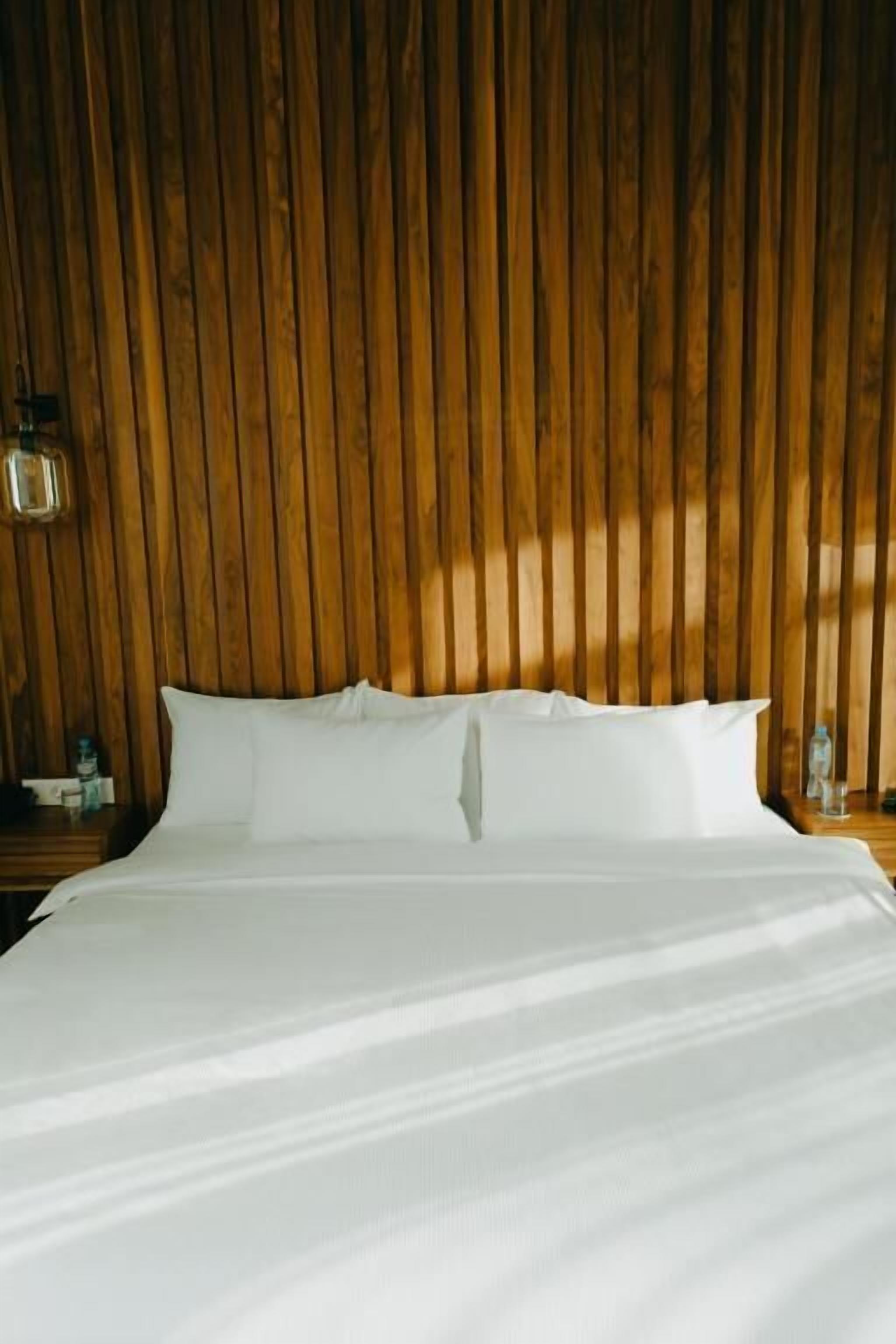 A bed with white linens, a wooden headboard, and a nightstand with a bottle.