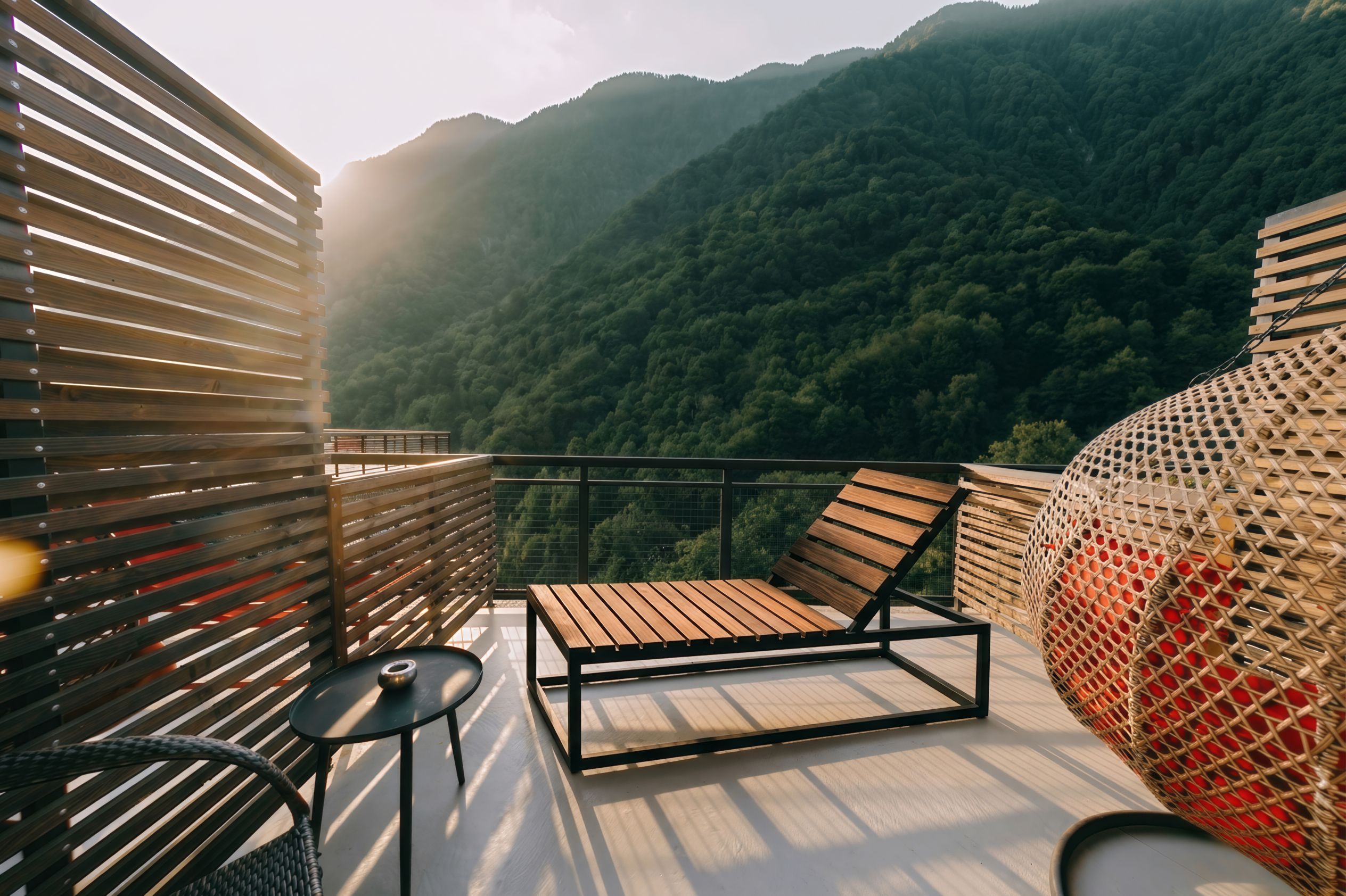 A balcony with a wooden chair and table, overlooking a forested mountain.