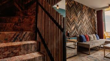 Un escalier avec des marches en bois et une rampe en métal, menant à une pièce dont un mur est décoré d’un motif en chevrons et qui contient un canapé avec des coussins.
