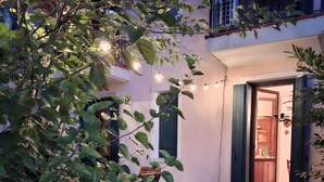 Um jardim com uma cadeira de madeira, entrada de casa e luzes de cordão.