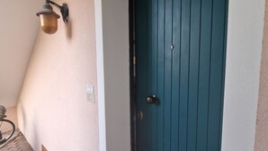 Uma porta verde-água com puxador de latão, luminária fixada na parede e chão de azulejos.