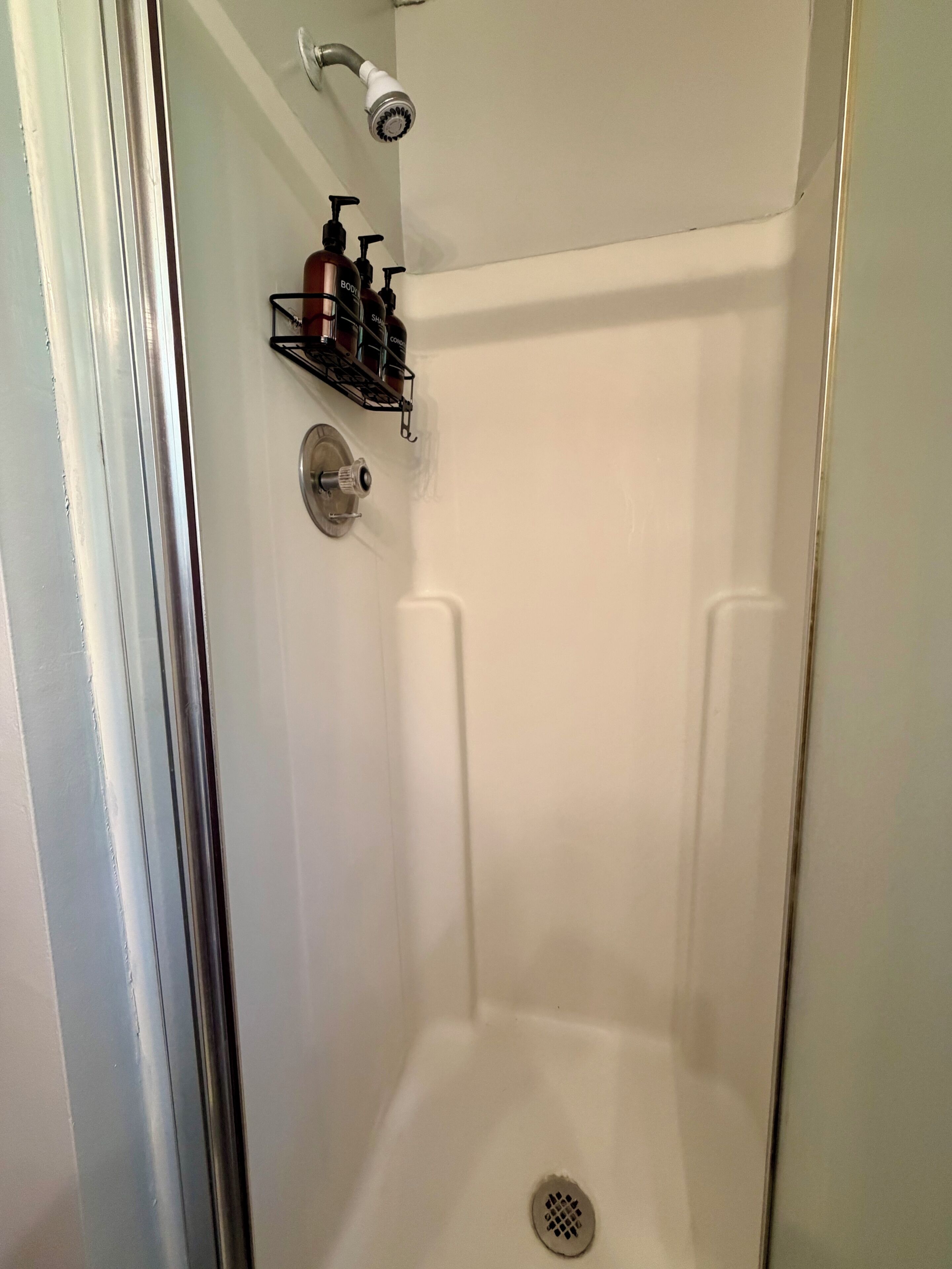 Une douche équipée d’un pommeau de douche à main, d’un robinet mural et d’une étagère pour les articles de toilette.