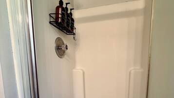Une douche équipée d’un pommeau de douche à main, d’un robinet mural et d’une étagère pour les articles de toilette.