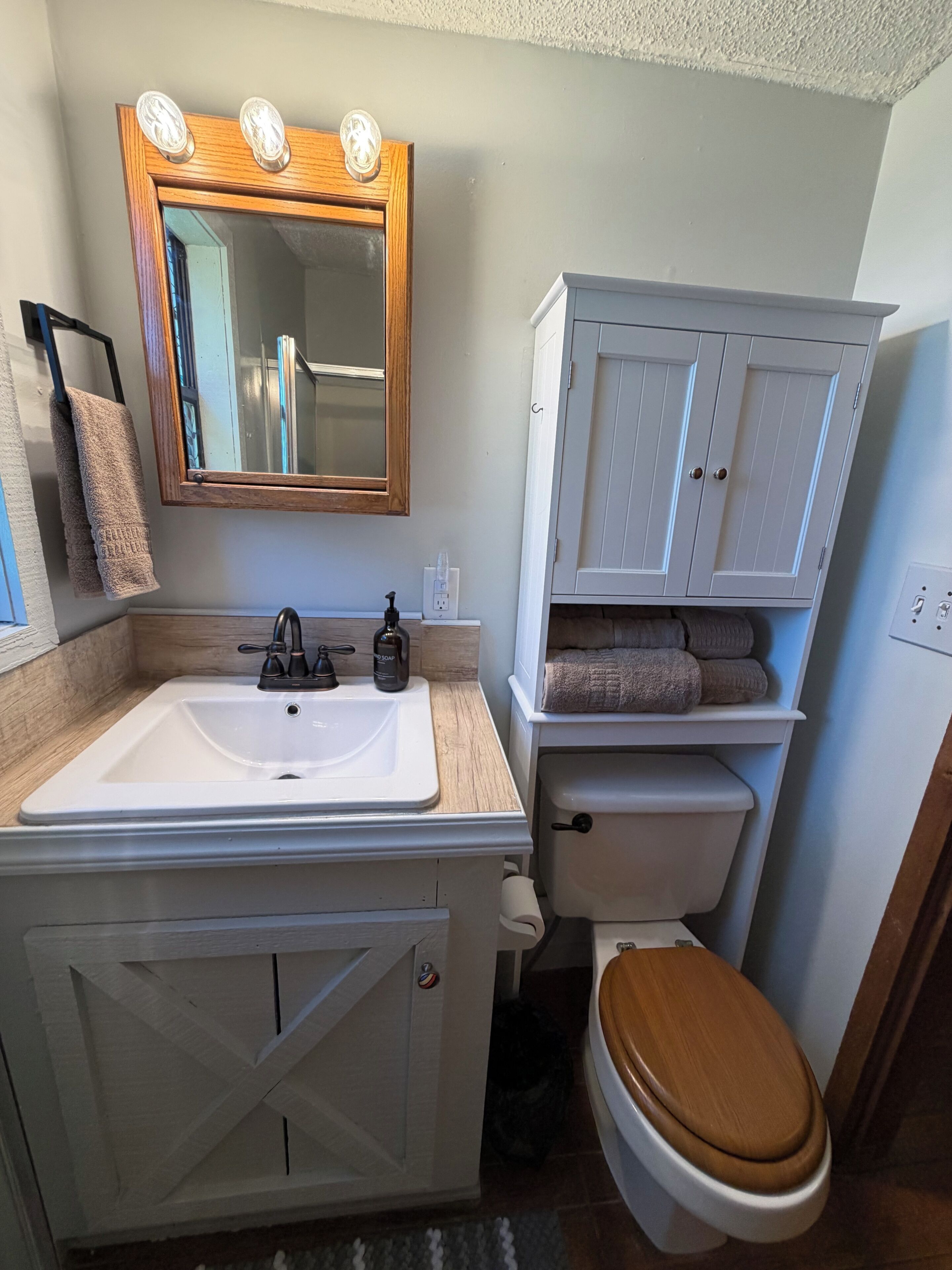Een badkamer met een wit wastafel, spiegel en toilet. Er liggen handdoeken en staat een zeepdispenser op het aanrecht.