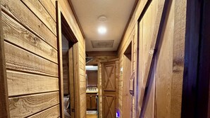 A narrow hallway with wooden walls and a patterned carpet, leading to a barn-like structure with a door.