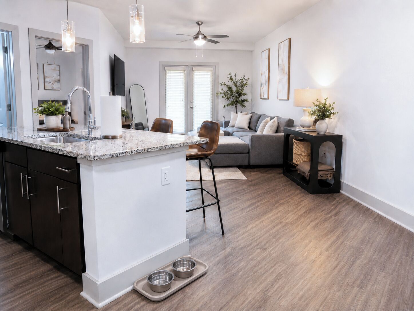 A modern kitchen with a granite countertop, a built-in sink, and a dining area with a grey sofa and a small side table.