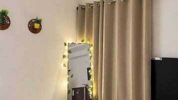 Een moderne badkamer met een grote spiegel, beige gordijnen, een potplant en een plafondlamp.