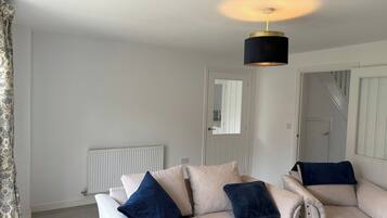 En stue med en hvid sofa, en sort hængende lampe og en radiator.