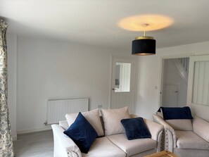 Un salon avec un ensemble de canapés blancs, un luminaire suspendu noir et un radiateur.