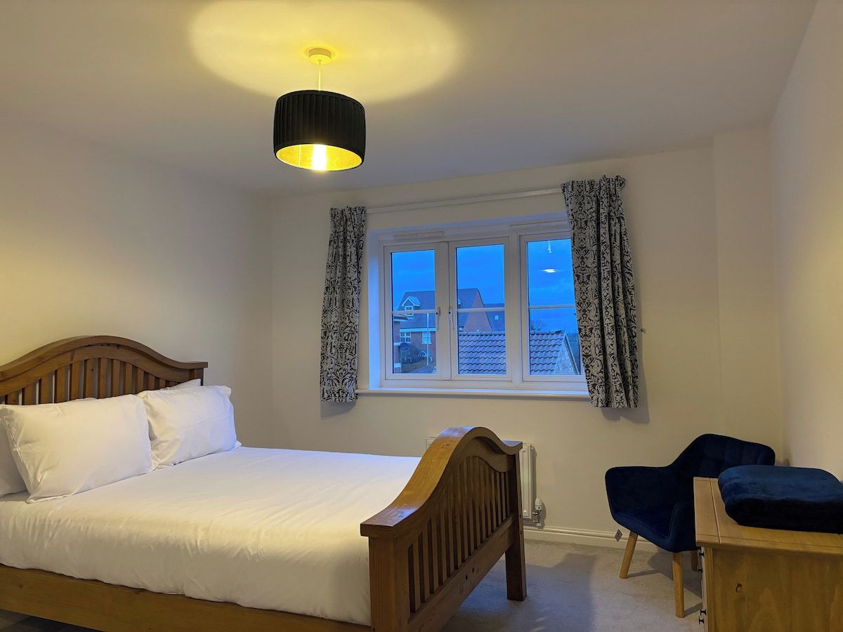 Une chambre à coucher comprenant un lit, un bureau, une chaise, une fenêtre avec des rideaux et un luminaire suspendu.