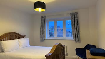 A bedroom with a bed, a desk, a chair, a window with curtains, and a hanging light fixture.
