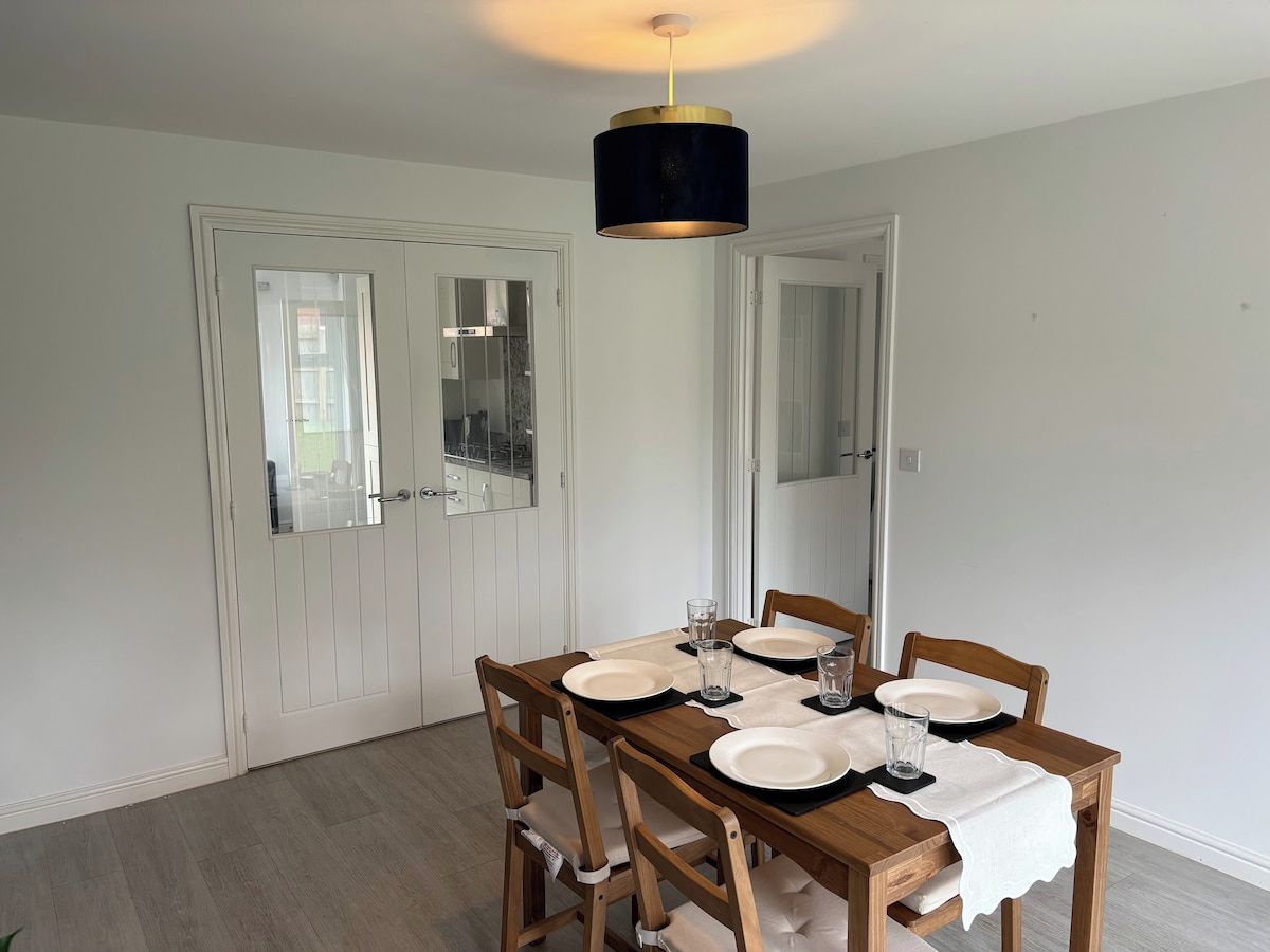 A dining area with a wooden table set for four, white walls, and a ceiling light fixture.