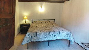 Et soveværelse med træloft, en seng med blomstret sengetæppe, et natbord med lampe og en trædør.