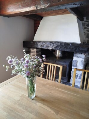 A wooden table with a vase of flowers, a stone fireplace, and a wooden chair. - Mountain cabin near Lake Annecy. Ideal for couples and families. No pets allowed. (Saint-Ferréol)