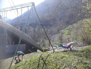 A rural outdoor setting with a swing set, a person on a swing, and a person lying on a lawn chair. - Mountain cabin near Lake Annecy. Ideal for couples and families. No pets allowed. (Saint-Ferréol)